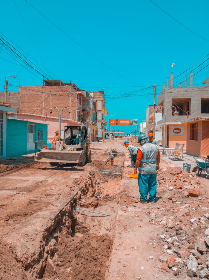 Workers engage in road construction under clear blue skies in a city street.